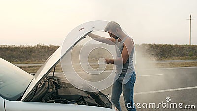 Ένα άτομο εξετάζει μια καπνίζοντας μηχανή ενός σπασμένου αυτοκινήτου Ένα άτομο εξετάζει μια καπνίζοντας μηχανή ενός σπασμένου αυτοκινήτου