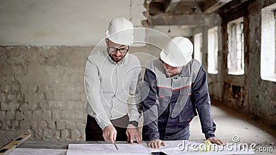 Ένας ενήλικος μηχανικός εξηγεί στον εργαζόμενο που ένα σχέδιο νέας κατασκευής, που σχεδιάστηκε από τον αρχιτέκτονα, άνθρωποι είνα απόθεμα βίντεο Ένας ενήλικος μηχανικός εξηγεί στον εργαζόμενο που ένα σχέδιο νέας κατασκευής, που σχεδιάστηκε από τον αρχιτέκτονα, άνθρωποι είνα απόθεμα βίντεο