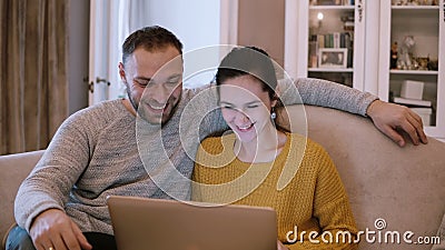 Νέο ζεύγος που κάνει σερφ το Διαδίκτυο με το lap-top καθμένος στον καναπέ στο καθιστικό και το γέλιο φιλμ μικρού μήκους Νέο ζεύγος που κάνει σερφ το Διαδίκτυο με το lap-top καθμένος στον καναπέ στο καθιστικό και το γέλιο φιλμ μικρού μήκους