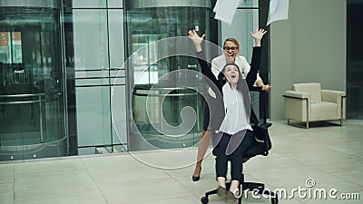 Замедленное движение жизнерадостных молодых женщин имея потеху в лобби офиса завихряясь вокруг сидеть в свертывая стуле и бросать видеоматериал Замедленное движение жизнерадостных молодых женщин имея потеху в лобби офиса завихряясь вокруг сидеть в свертывая стуле и бросать видеоматериал