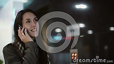 Молодая женщина стоя в зале офиса и говоря на телефоне Женщина используя smartphone и улыбку сток-видео Молодая женщина стоя в зале офиса и говоря на телефоне Женщина используя smartphone и улыбку сток-видео