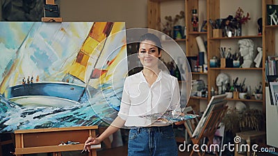 Портрет уверенного положения палитры и paintbrush удерживания художника девушки около seascape смотря камеру и усмехаться сток-видео Портрет уверенного положения палитры и paintbrush удерживания художника девушки около seascape смотря камеру и усмехаться сток-видео