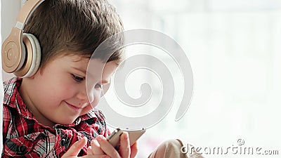Ребенок в наушниках, ребенк играя с smartphone и слушая к музыке через беспроволочные наушники сток-видео Ребенок в наушниках, ребенк играя с smartphone и слушая к музыке через беспроволочные наушники сток-видео