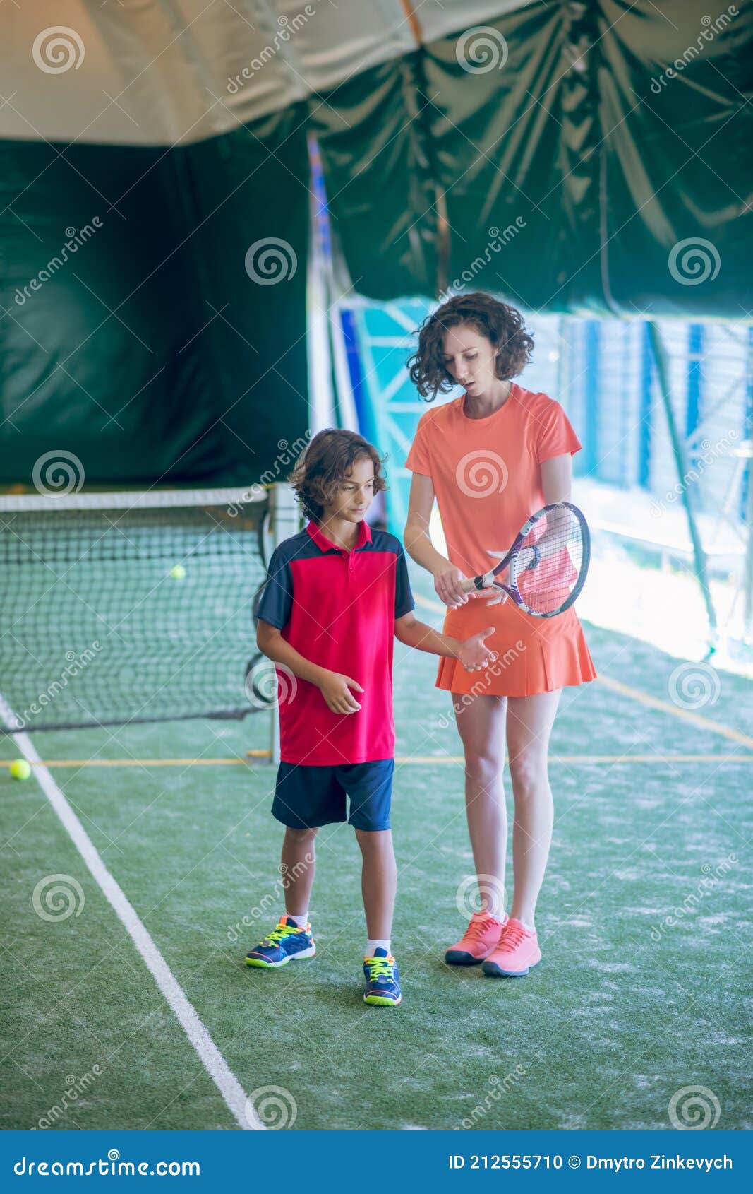 θηλυκό προπονητής με λαμπερά ρούχα μαθαίνει σε ένα αγόρι να κρατά μια  ρακέτα τένις Στοκ Εικόνες - εικόνα από lifestyle: 212555710
