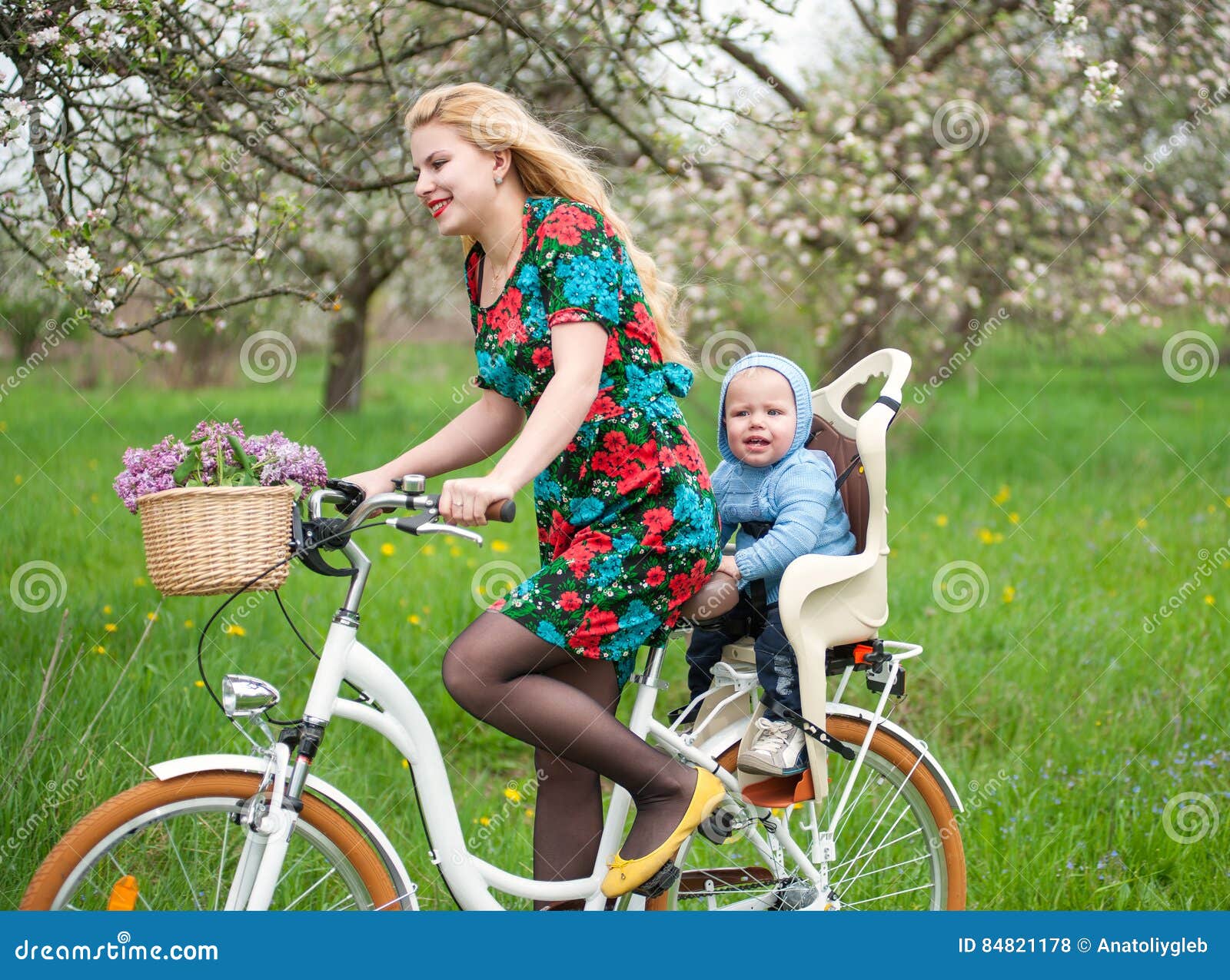 Ξανθό θηλυκό οδηγώντας ποδήλατο πόλεων με το μωρό στην καρέκλα ποδηλάτων  Στοκ Εικόνες - εικόνα από babylonia, lifestyle: 84821178