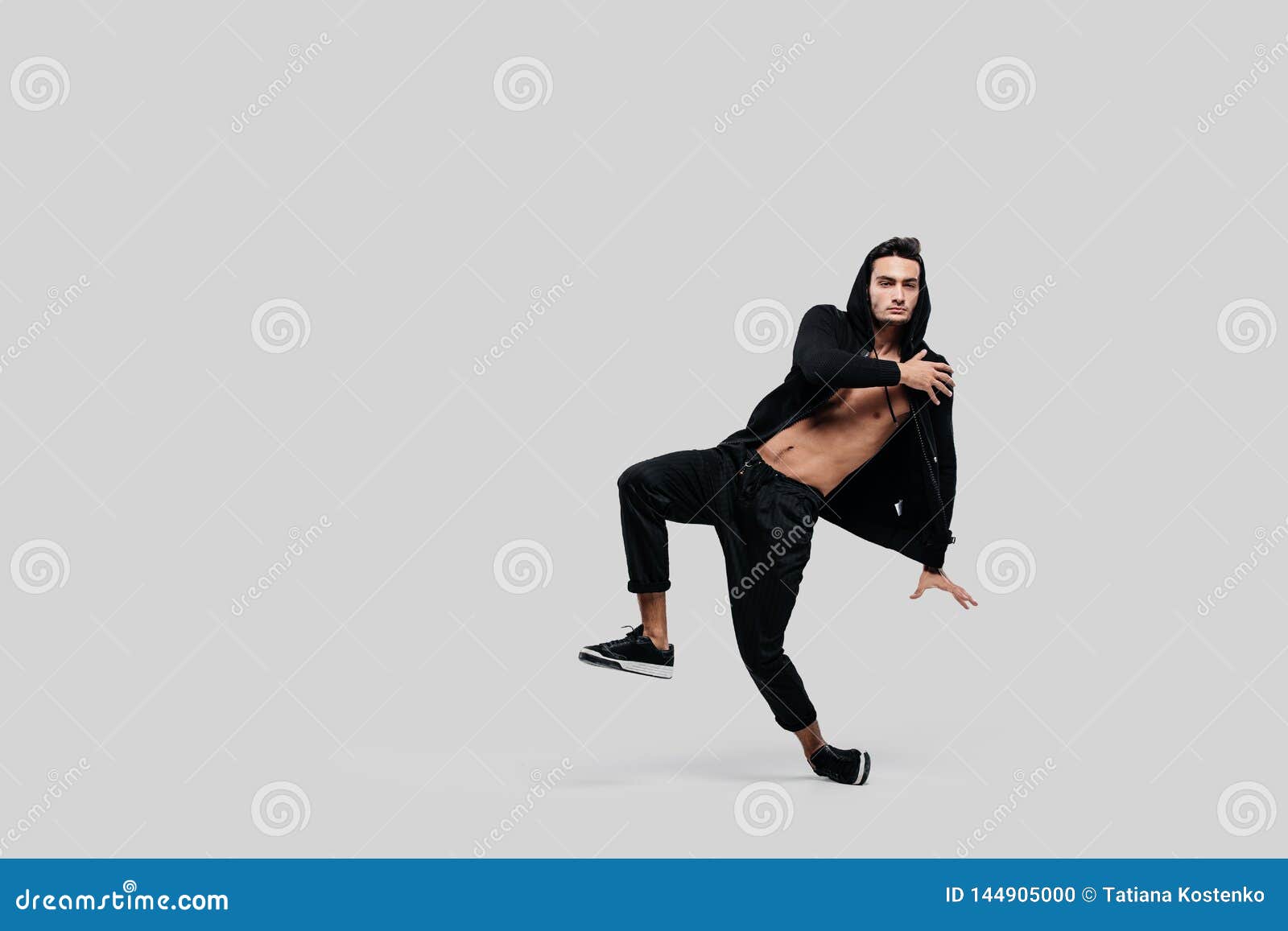 Ο όμορφος νέος χορευτής του χορού οδών που ντύνεται στα μαύρα εσώρουχα, μια  μπλούζα σε έναν γυμνό κορμό και μια κουκούλα χορεύει Στοκ Εικόνες - εικόνα  από lifestyle: 144905000