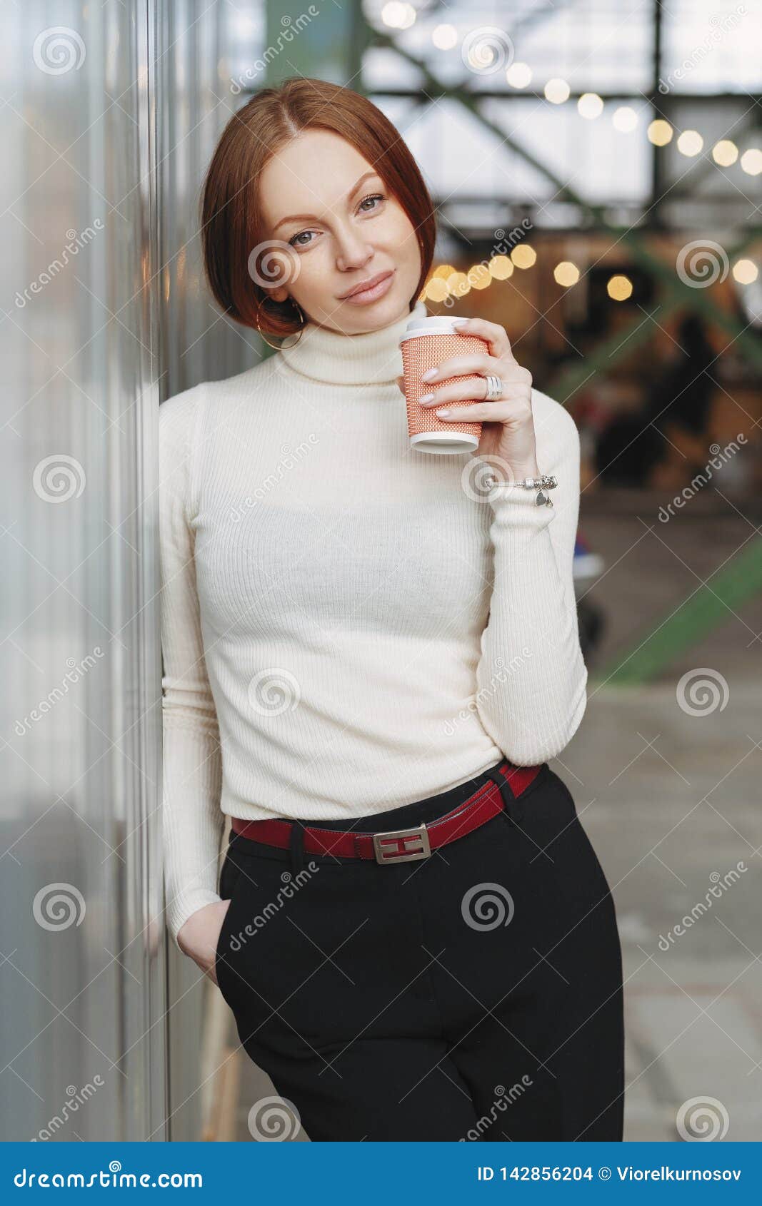 Вертикальное изображение внимательной молодой женщины носит белого прыгуна  и черные брюки, держат на вынос кофе, мечты о том, что Стоковое Фото -  изображение насчитывающей отдых, индивидуально: 142856204