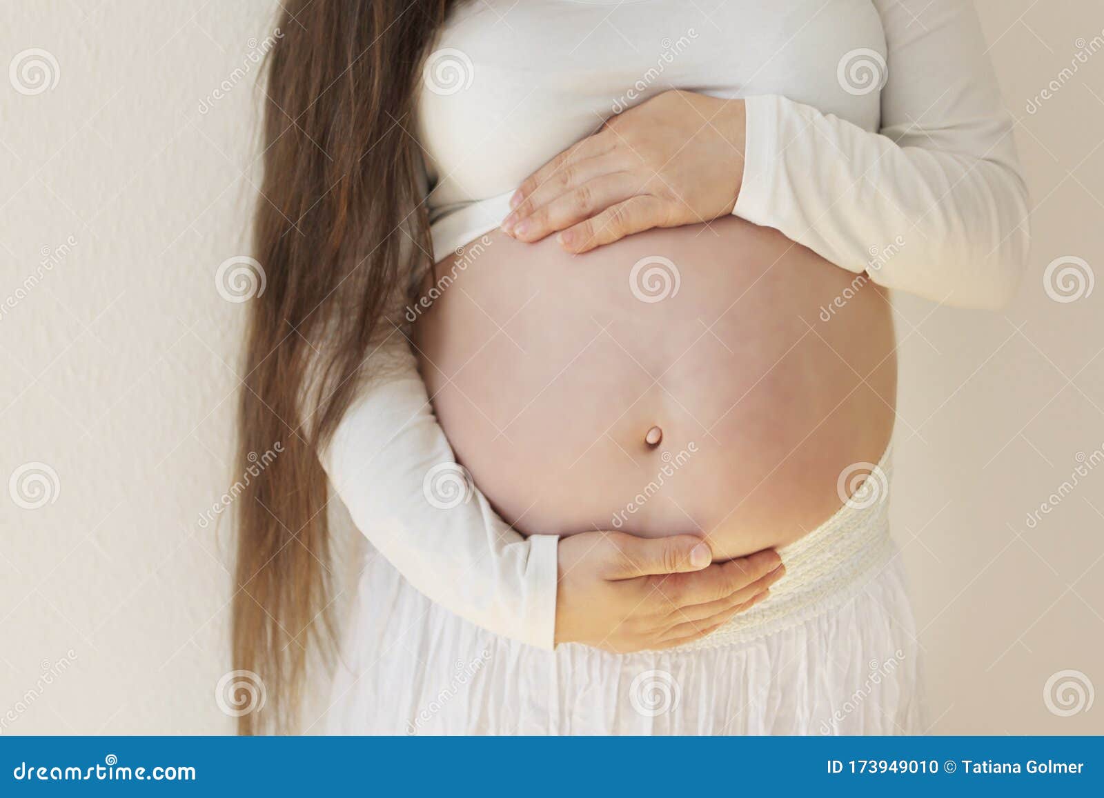 Голый большой живот беременной девушки в белых одеждах, которая держит его внимательно на светлой концепции фона безопасной береме Стоковое Фото - изображение насчитывающей образование, счастливо: 173949010
