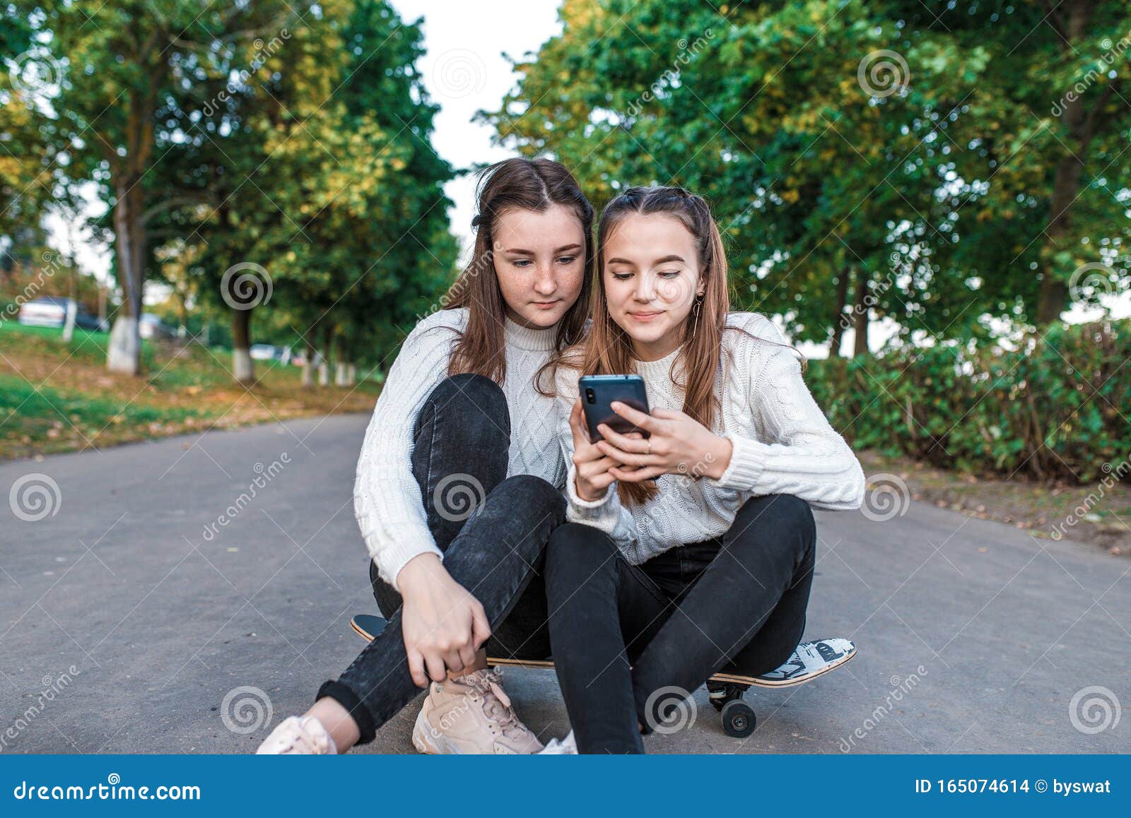 Две девочки-подростки, лучшие подруги, летний парк, сидящие на скейтборде,  смотрящие забавные видео смартфон, счастливые Стоковое Фото - изображение  насчитывающей интернет, приятельство: 165074614
