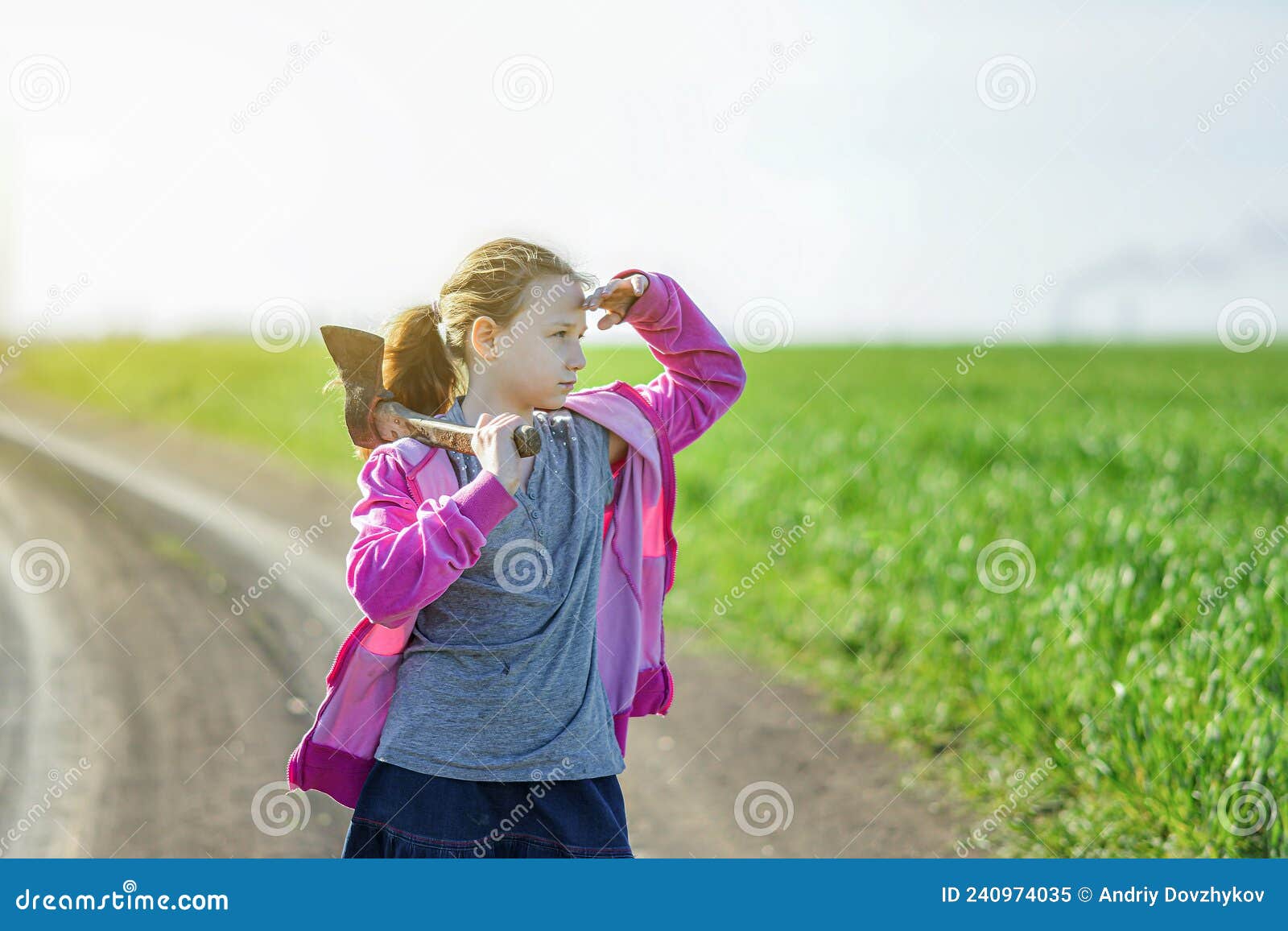 Девушка с топором на плече на фоне зелёного поля закрывает глаза от солнца и смотрит вперед Стоковое Изображение - изображение насчитывающей лесоруб, счастье: 240974035