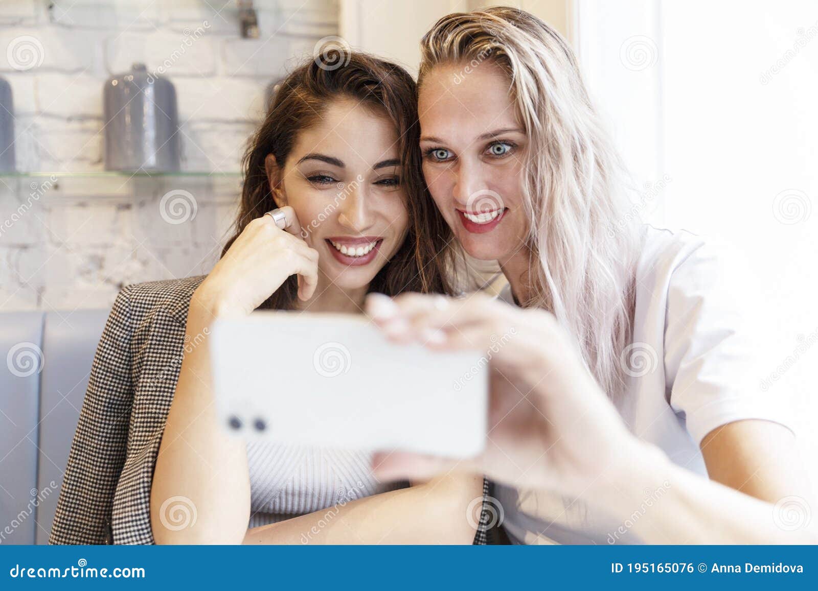 Девушки берут Selfie, сидя за столом в кафе. Молодые женщины блондинка и  брюнетка с улыбкой. Дружба и Стоковое Фото - изображение насчитывающей  смеяться, отдых: 195165076