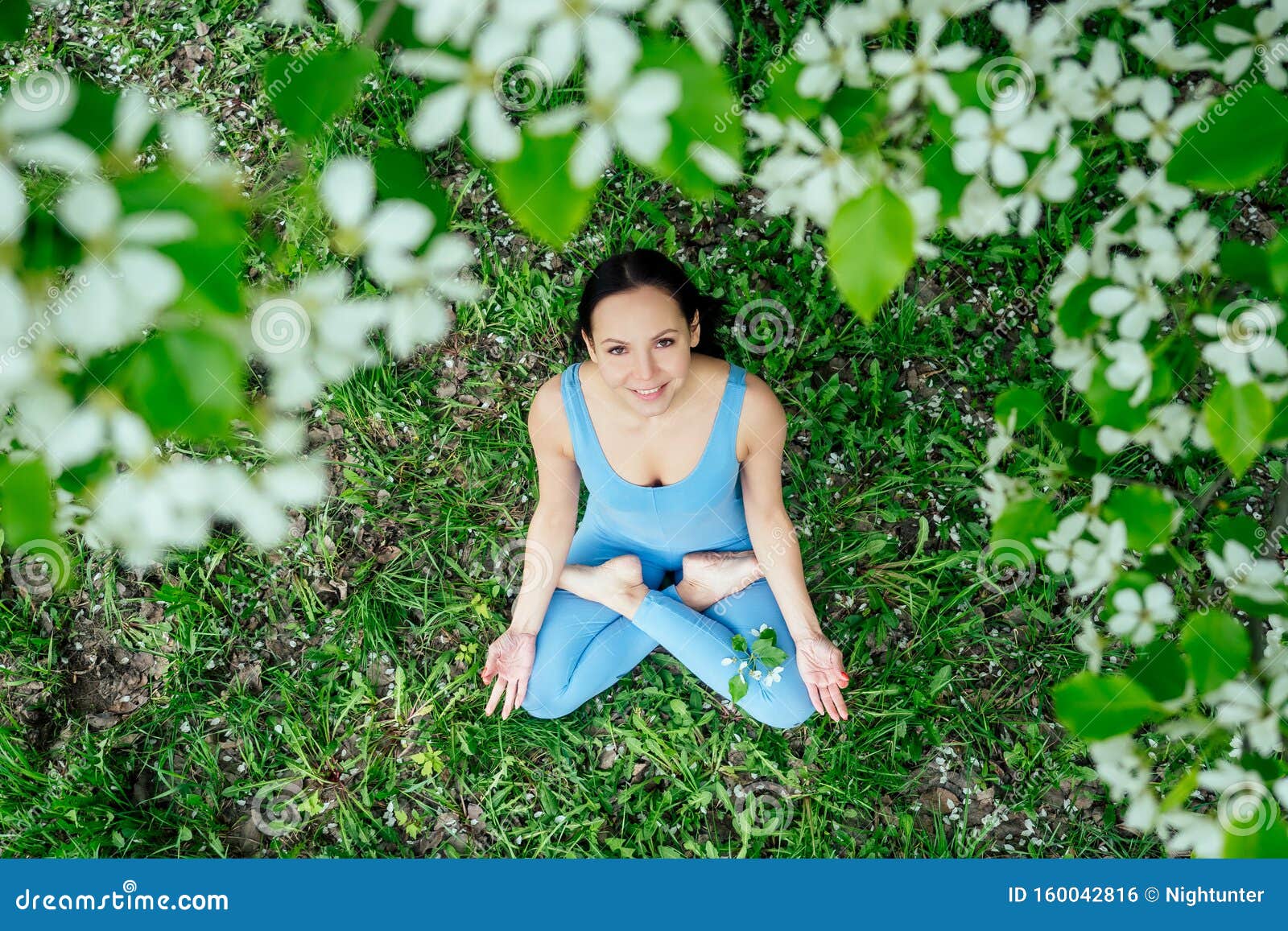 Красивая брюнетка в спортивном синем костюме на фоне цветущих весенних деревьев, сидящих на зеленой траве Стоковое Фото - изображение насчитывающей цветок, счастливо: 160042816