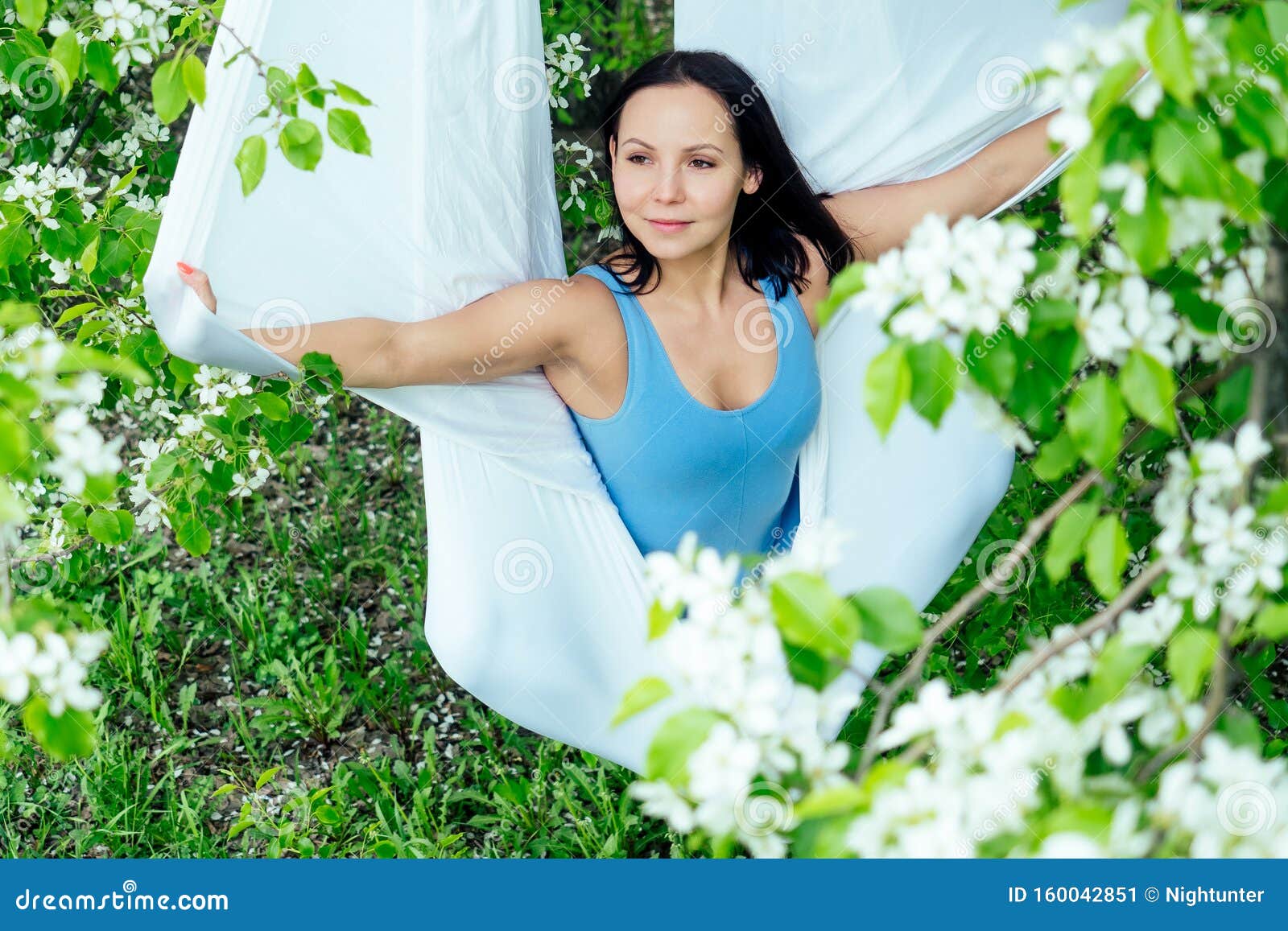 Красивая брюнетка в спортивном синем костюме на фоне цветущих весенних деревьев, занятых антигравитацией Стоковое Изображение - изображение насчитывающей мантра, актеров: 160042851