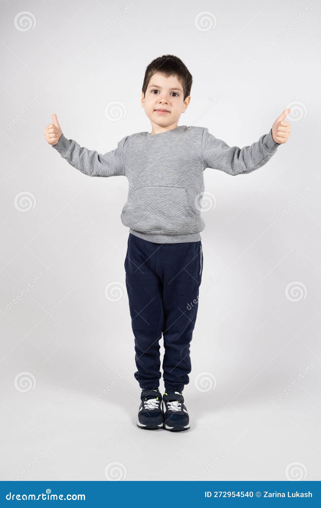 маленький мальчик в свитерных брюках и кроссовках, показывающих большие пальцы на белом фоне. одежда для детей Стоковое Фото - изображение насчитывающей мило, представлять: 272954540