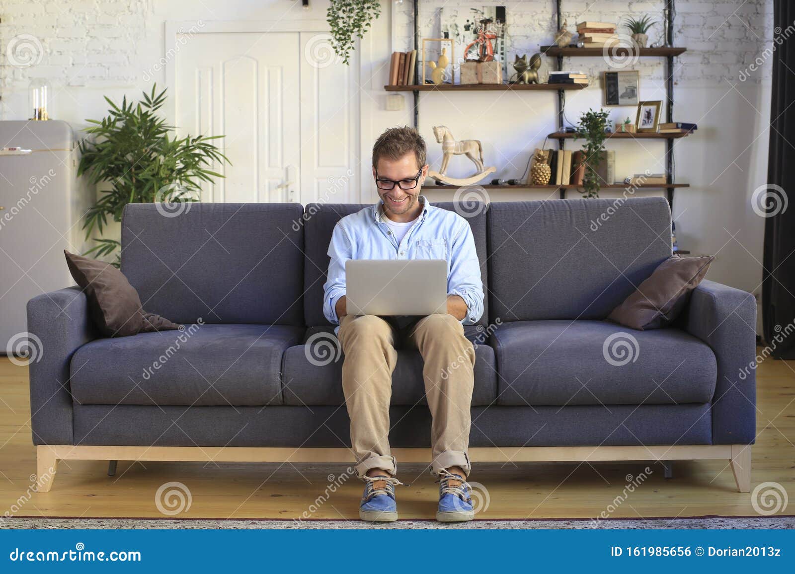 Молодой человек сидит и работает на диване с ноутбуком Стоковое Фото -изображение насчитывающей тетрадь, пол: 161985656