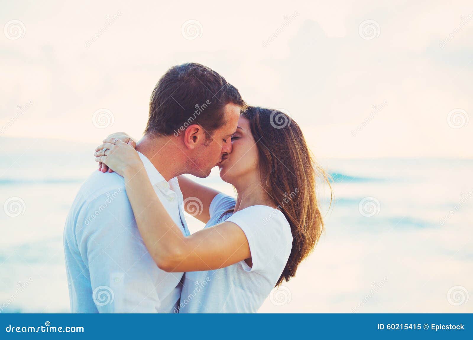 Молодая пара целуются на бежевом фоне. Восход и молодые пары целуются. Белая футболка с поцелуями. Пары целуются в Греции.