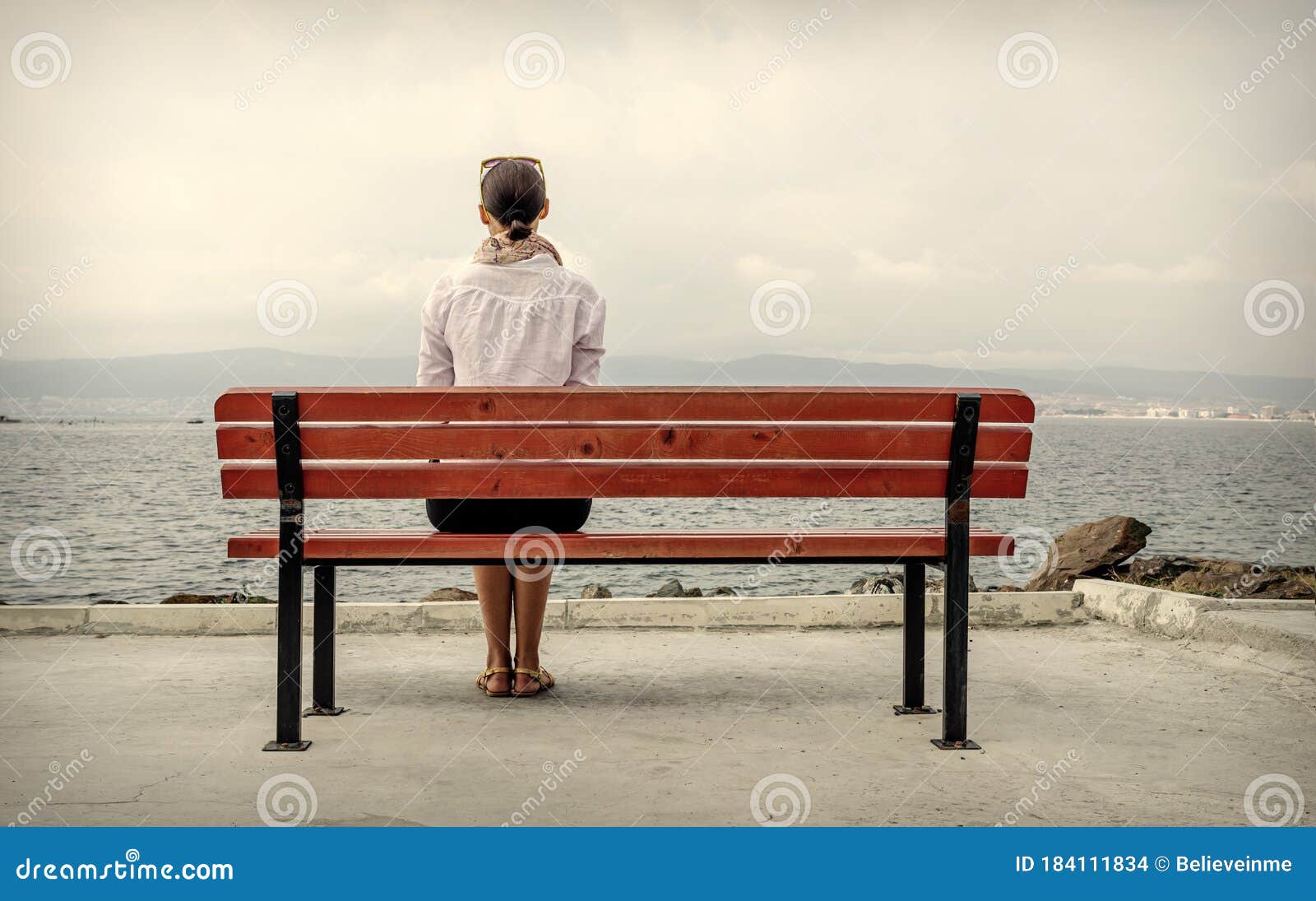Одинокая женщина сидит на скамейке водой. Тонизированное изображение.  Стоковое Фото - изображение насчитывающей красивейшее, повелительница:  184111834