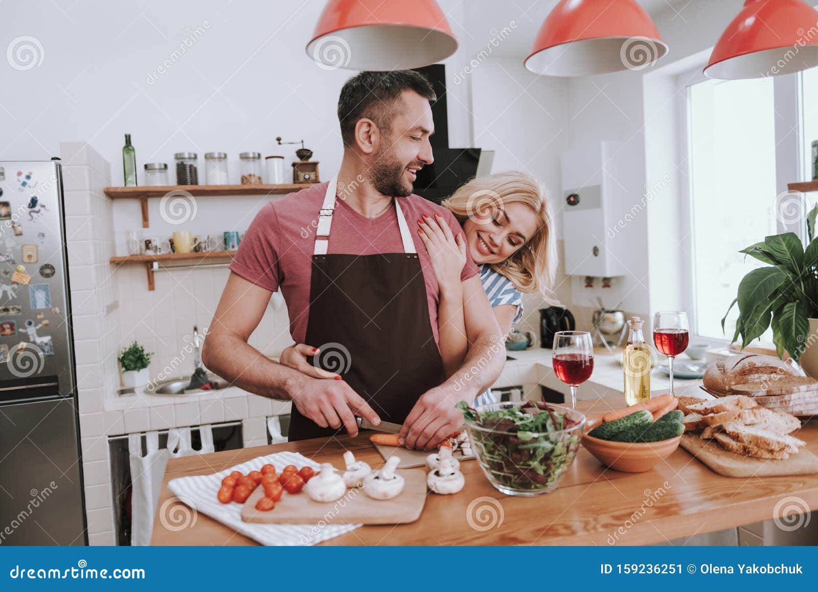 Пока жена готовит муж. Муж готовит ужин. Муж обнимает жену на кухне. Мужчина готовит женщина обнимает. Мужчина готовит на кухне женщина обнимает.