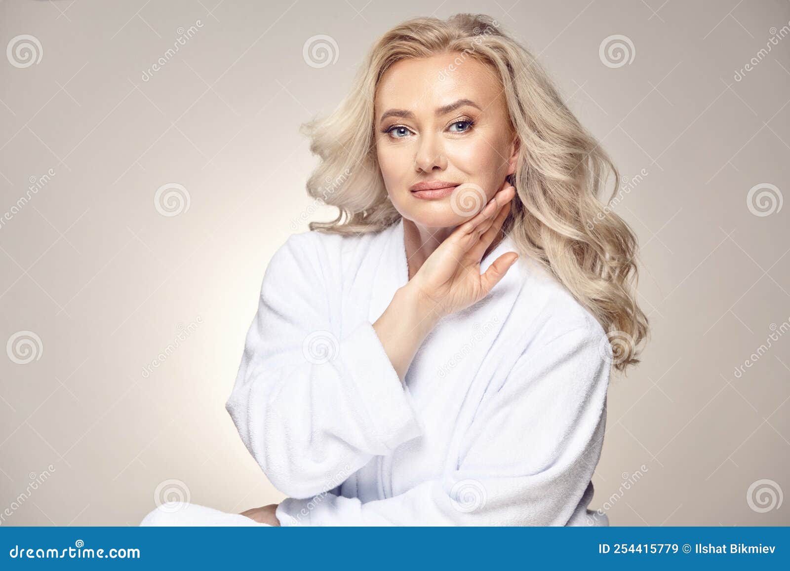 очаровательная красавица блондинка в возрасте пятидесяти лет, одетая в  спа-халат, положила руку на лицо, чистоту Стоковое Изображение -  изображение насчитывающей чисто, изолировано: 254415779