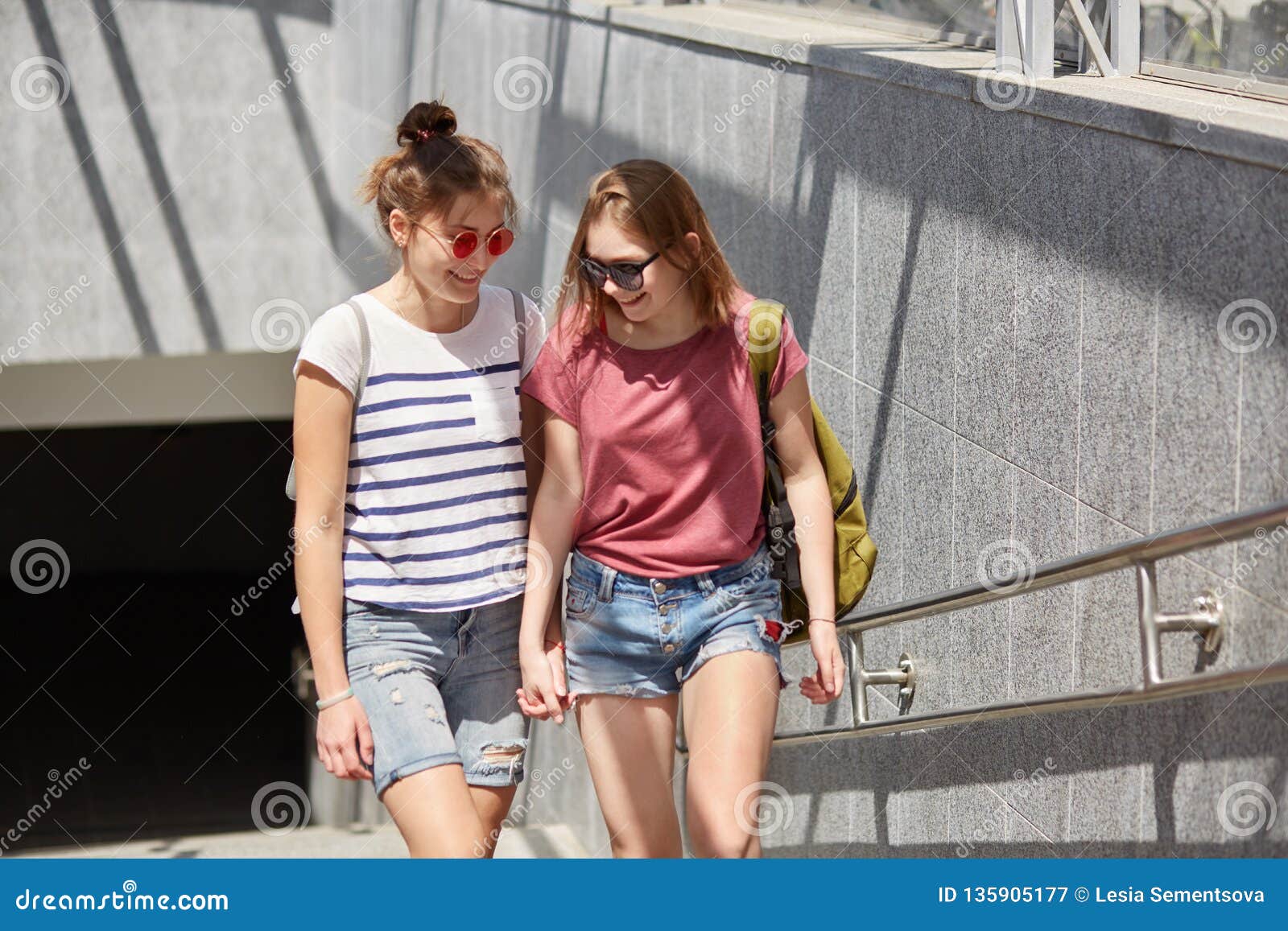 Положительные лесбиянки маленьких девочек держат руки, носят рюкзак,  случайную футболку и шорты, идут около подземного имеют бесе Стоковое  Изображение - изображение насчитывающей романтично, аффекты: 135905177