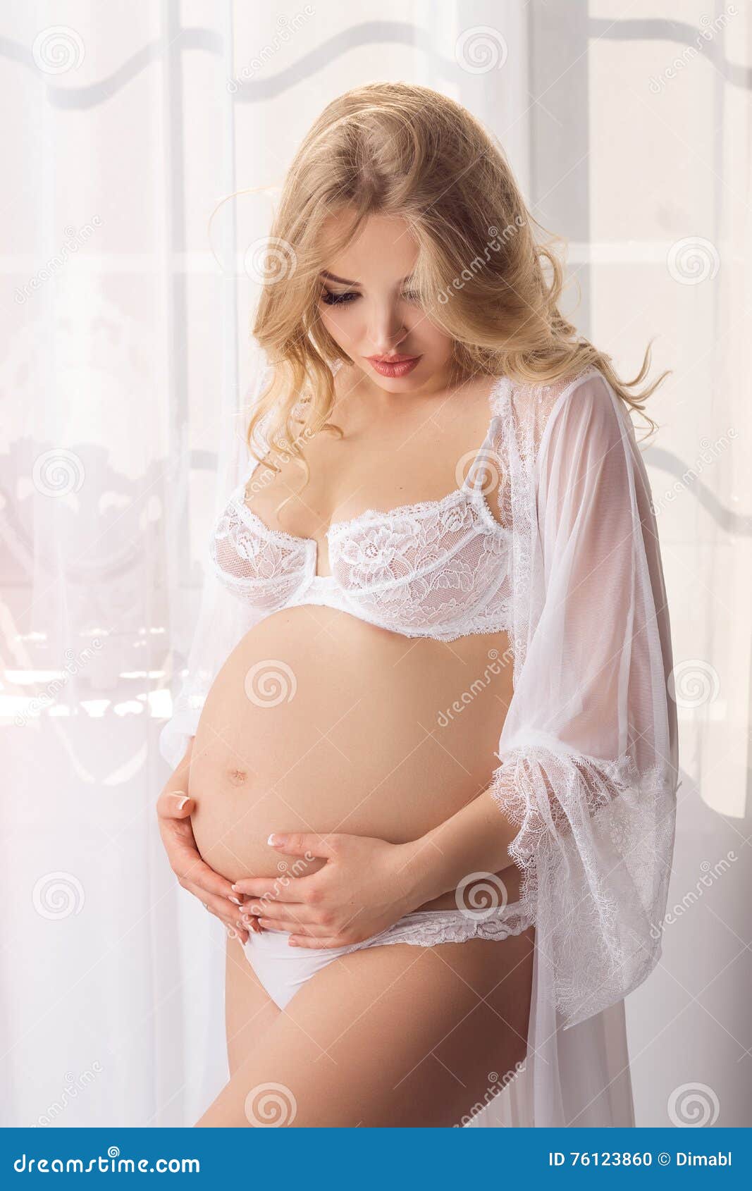 Привлекательная молодая белокурая беременная женщина представляя в белом же...