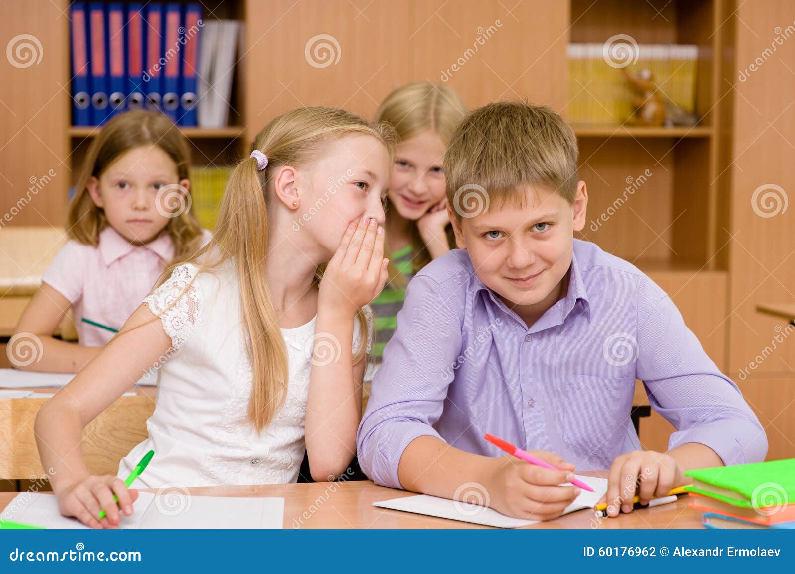 Русская дает одноклассникам. Ученики шепчутся. Шепчутся на уроке. Дети сидят за партой. Школьники шепчутся на уроке.