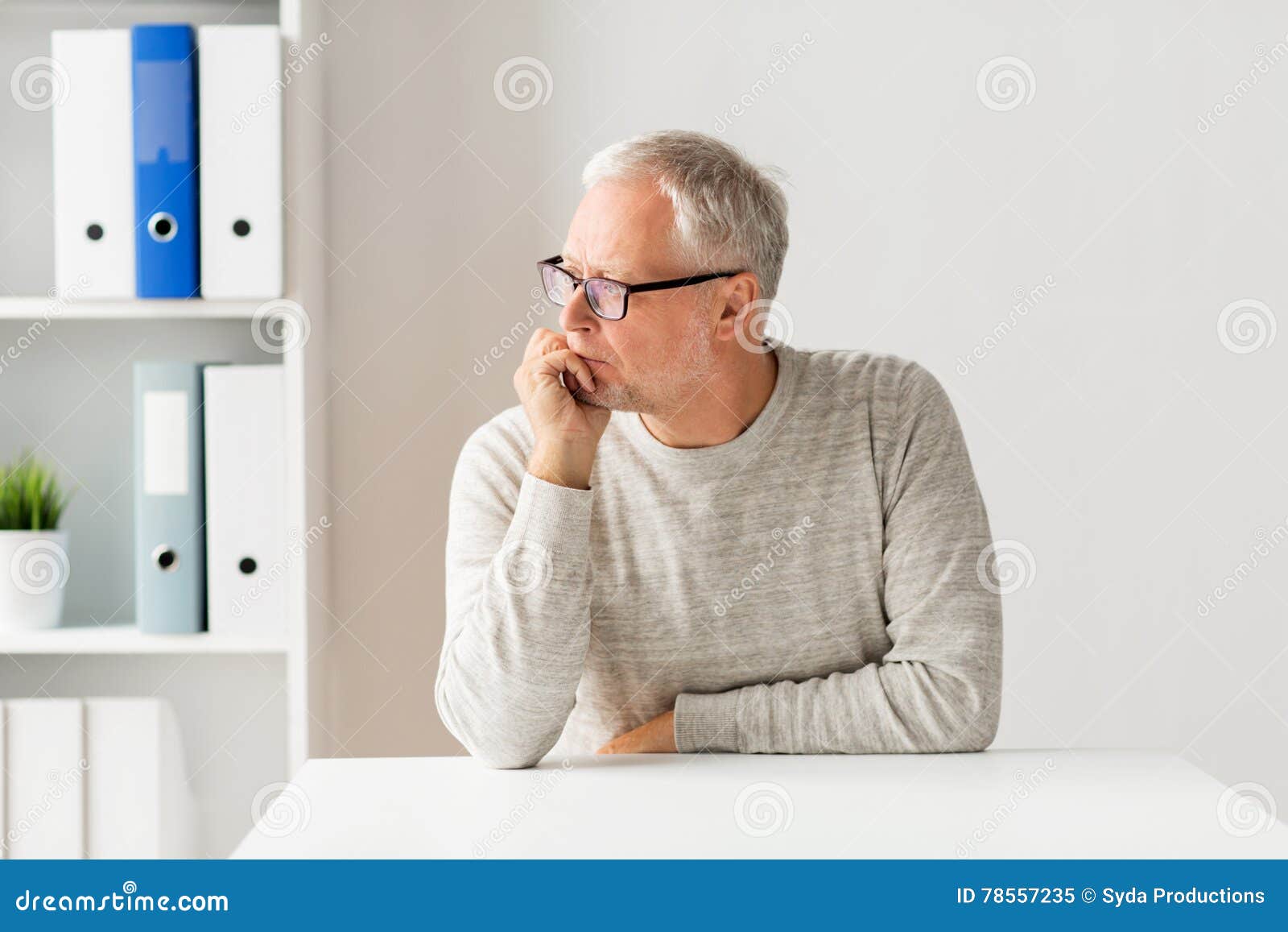 В скромно обставленном кабинете сидел пожилой человек. Пожилой мужчина за столом. Пожилой мужчина сидит за столом. Старик сидит за столом. Пожилой мужчина в офисе.