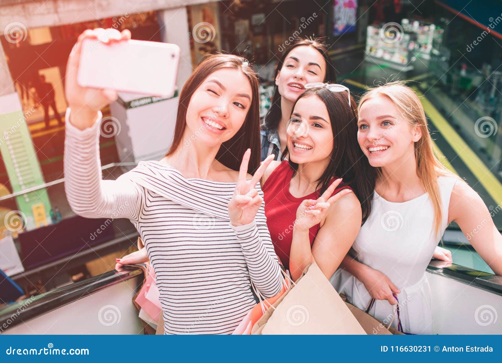 Хорошая женская компания стоит совместно на эскалаторе и принимает Selfie  Они смотрят телефон и усмехаться азиатско Стоковое Изображение -  изображение насчитывающей кавказско, мол: 116630231