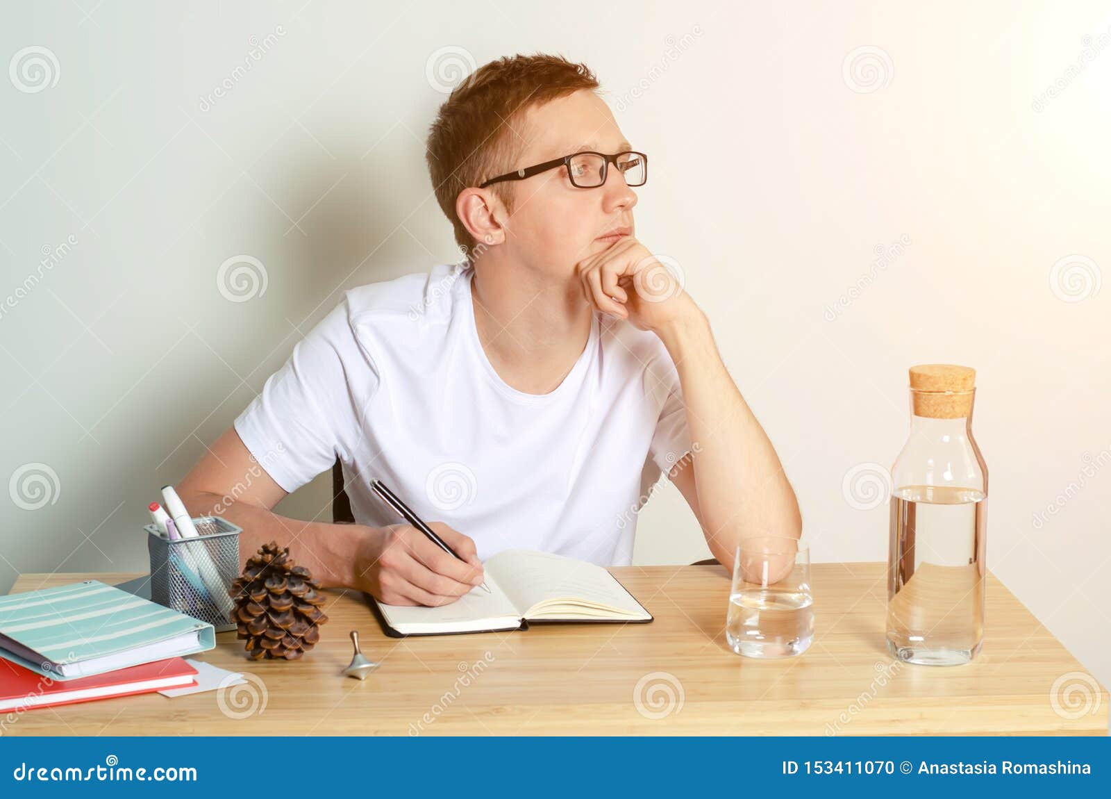 一位身穿白色t恤衫的年轻男子坐在办公桌前 在笔记本上写东西库存照片 图片包括有 153411070