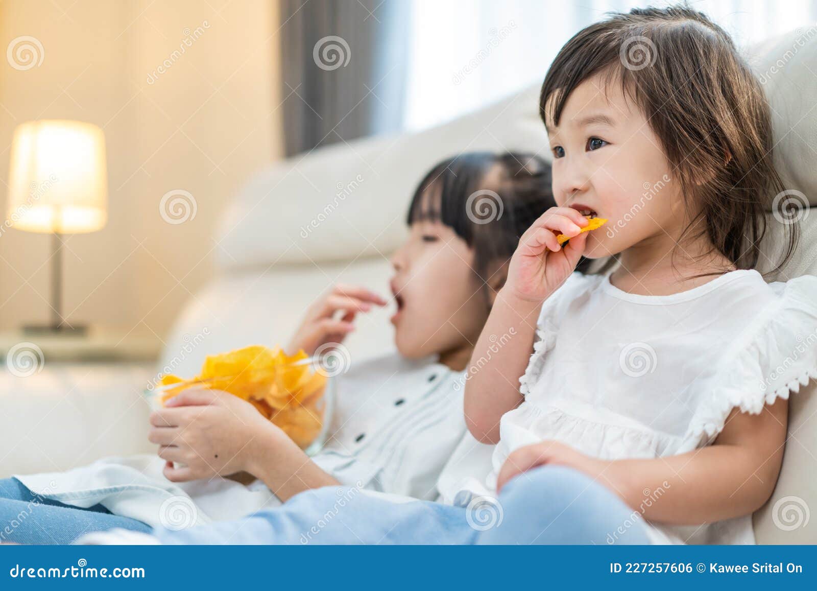 亚洲饥饿的小姐姐带手吃零食. 两个在沙发上休息的甜美的学前儿童可以  image