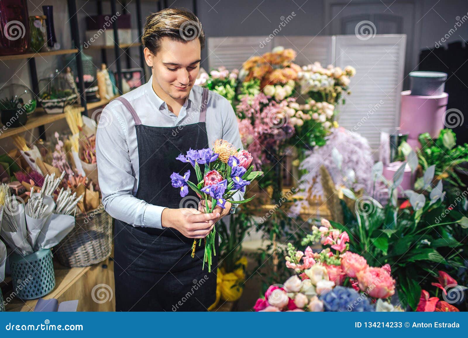 快乐的年轻男性卖花人举行五颜六色的花束在手上他看它不同的植物和花是在他后库存图片 图片包括有存储 丝带