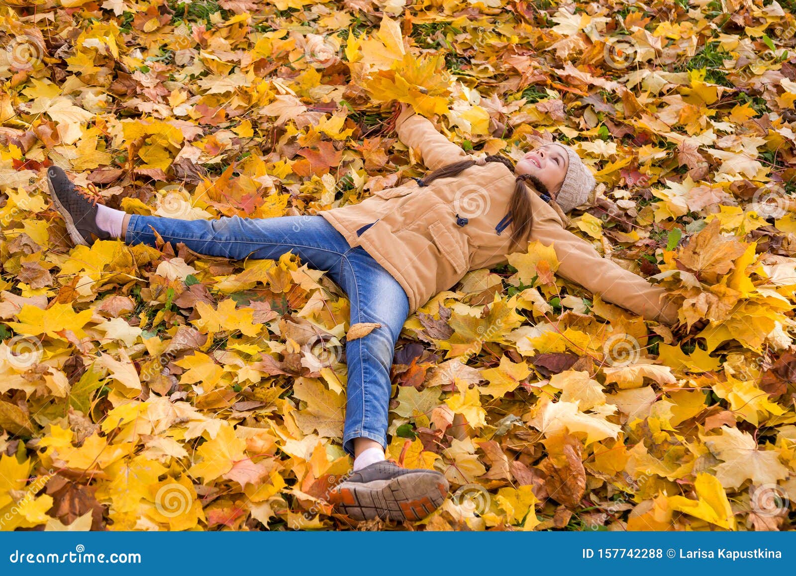 躺在落叶上的快乐小女孩伸出双臂 手中捧着黄枫叶的花束库存照片 图片包括有