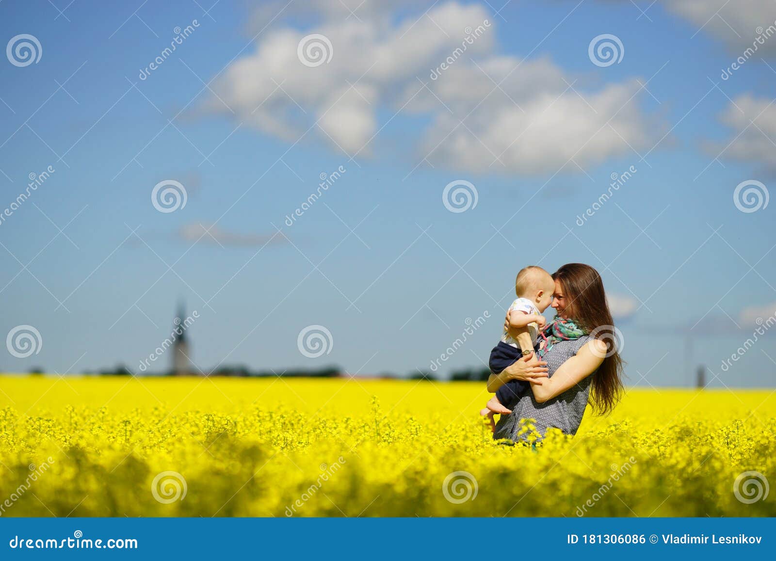 阳光明媚的夏日 艳蓝的天空 黄的草甸 在鲜黄的花田里 年轻母亲手抱着孩子库存照片 图片包括有幸福 父项