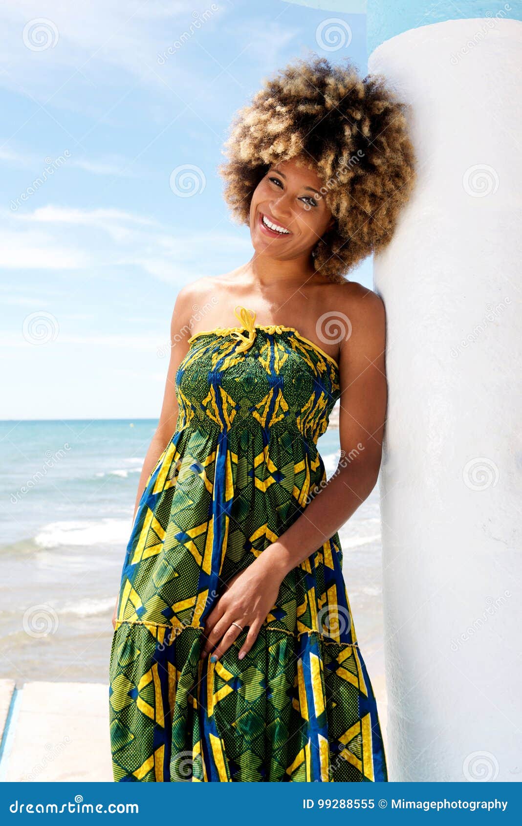 Portret van aantrekkelijk Afrikaans model die tegen muur in een kleding bij strand leunen