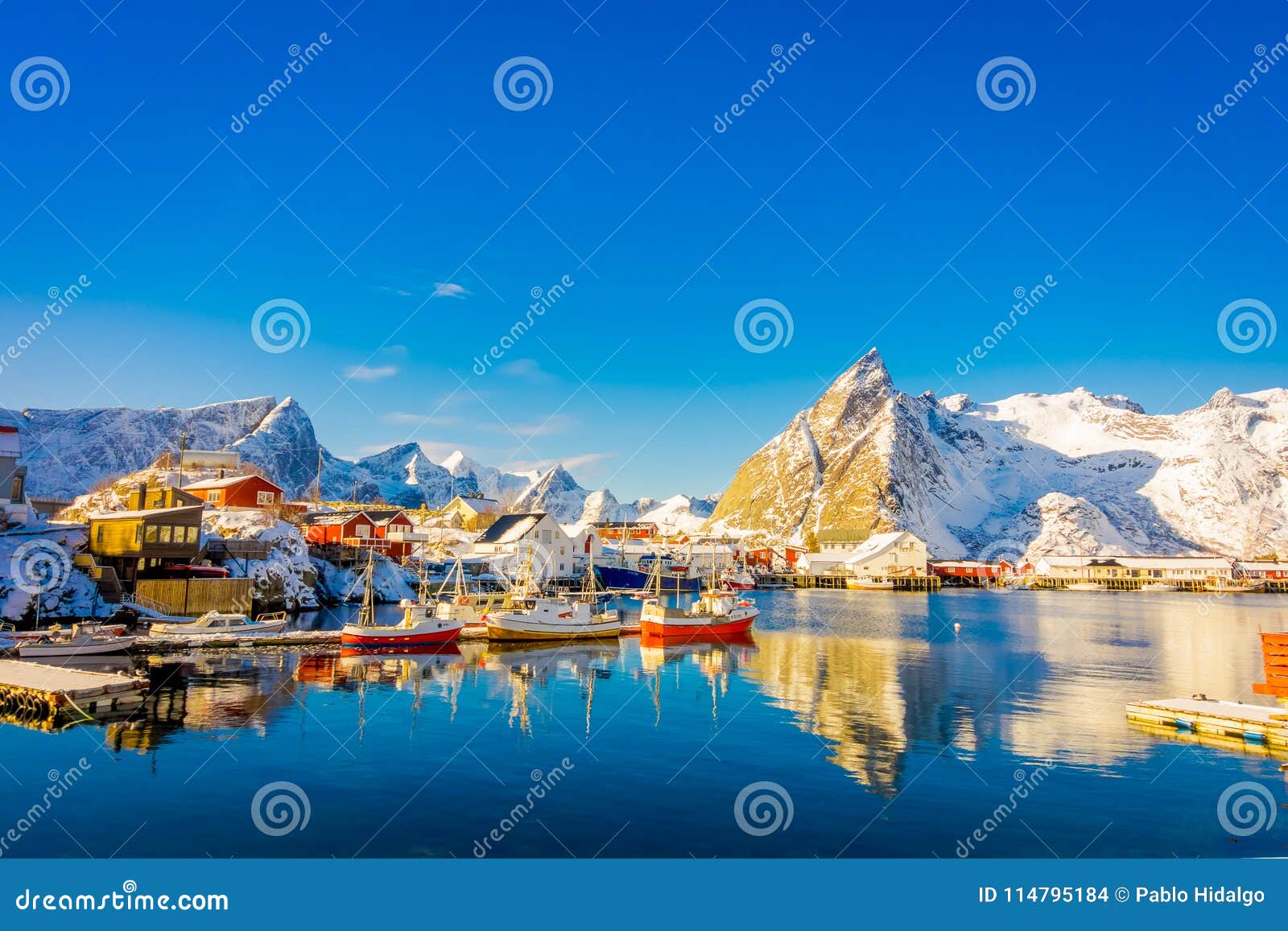 above view of some wooden buildings in the bay with boats in the shore in lofoten islands surrounded with snowy