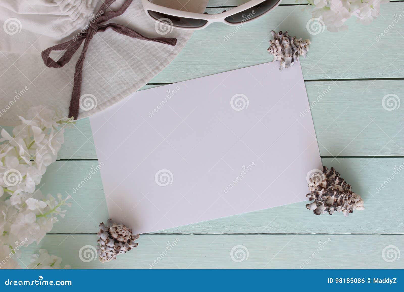 Accesorios de la playa en el tablero de madera de la turquesa azul clara conchas marinas, sombrero y vidrios, algunas flores Hoja de papel en blanco para el espacio de la copia