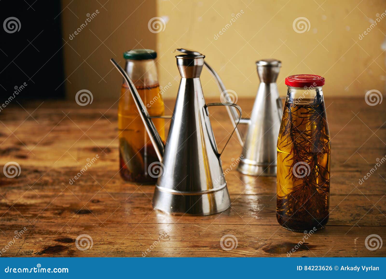 Aceite de oliva con las hierbas y los dispensadores de acero. Dos botellas con el hogar del artesano hicieron el aceite de oliva picante con romero y las pimientas y dos vinagreras brillantes del metal en una tabla marrón áspera