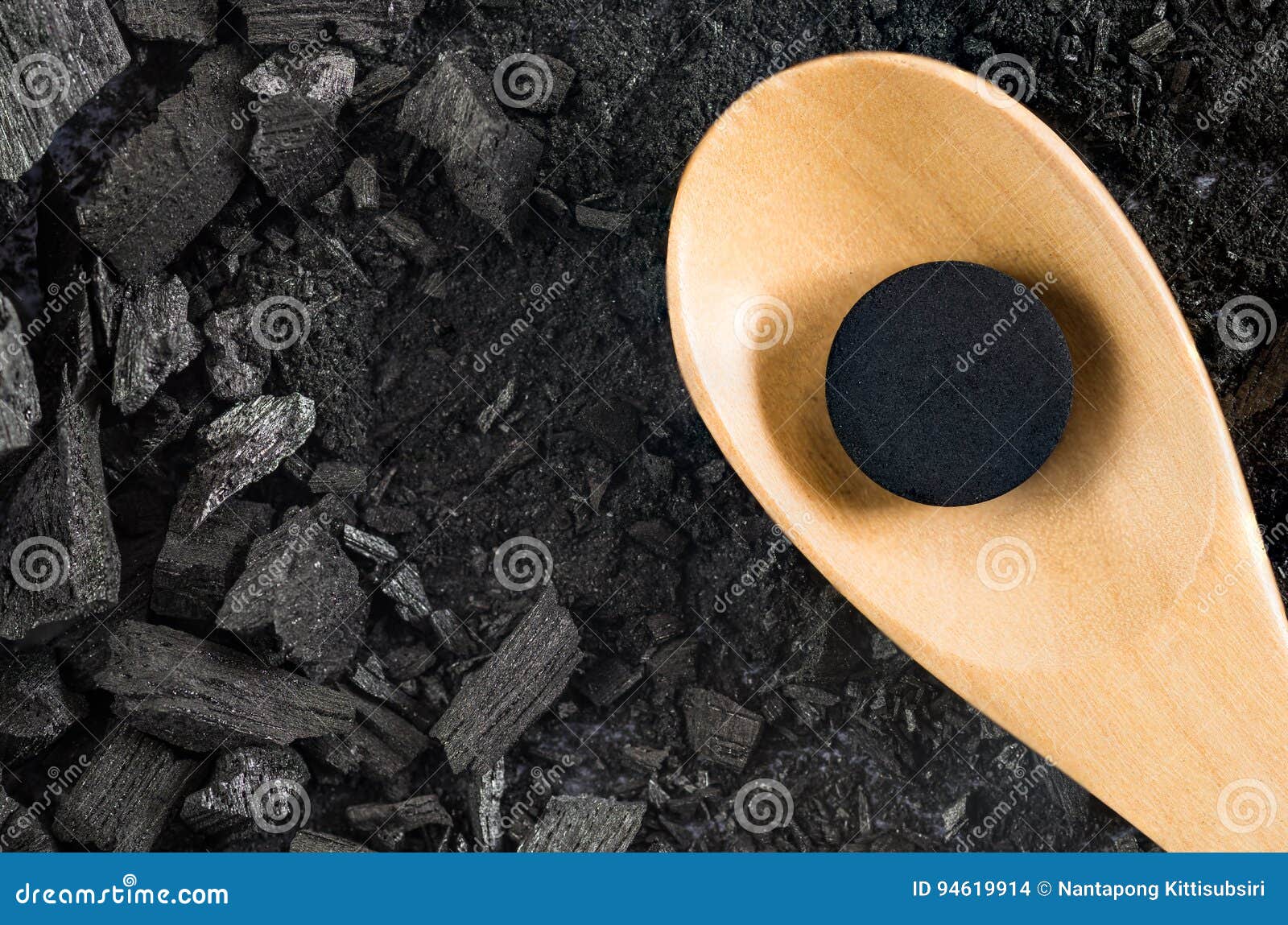 activated carbon pill medicine in wooden spoon on ground charcoal