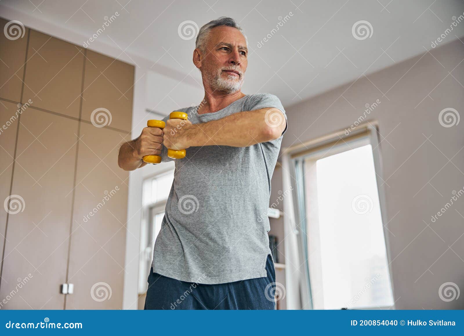enthusiastic elderly man working out with dumbbells at home