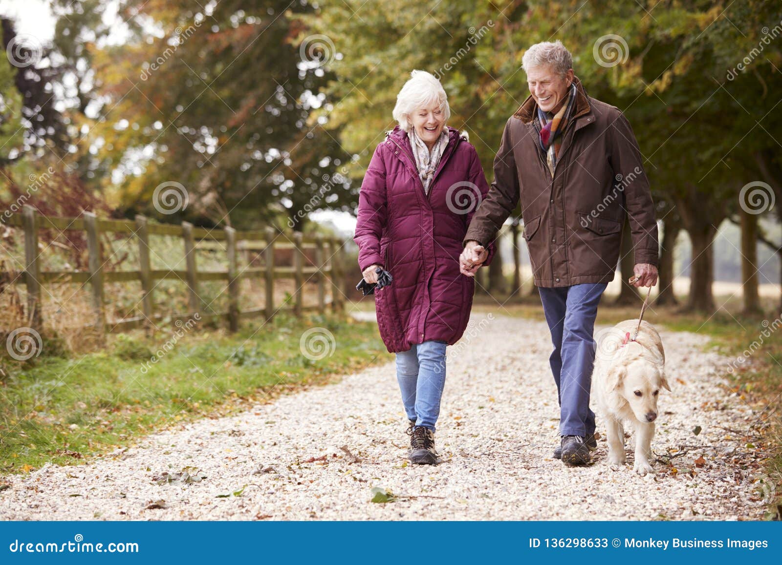 active senior couple on autumn walk with dog on path through countryside