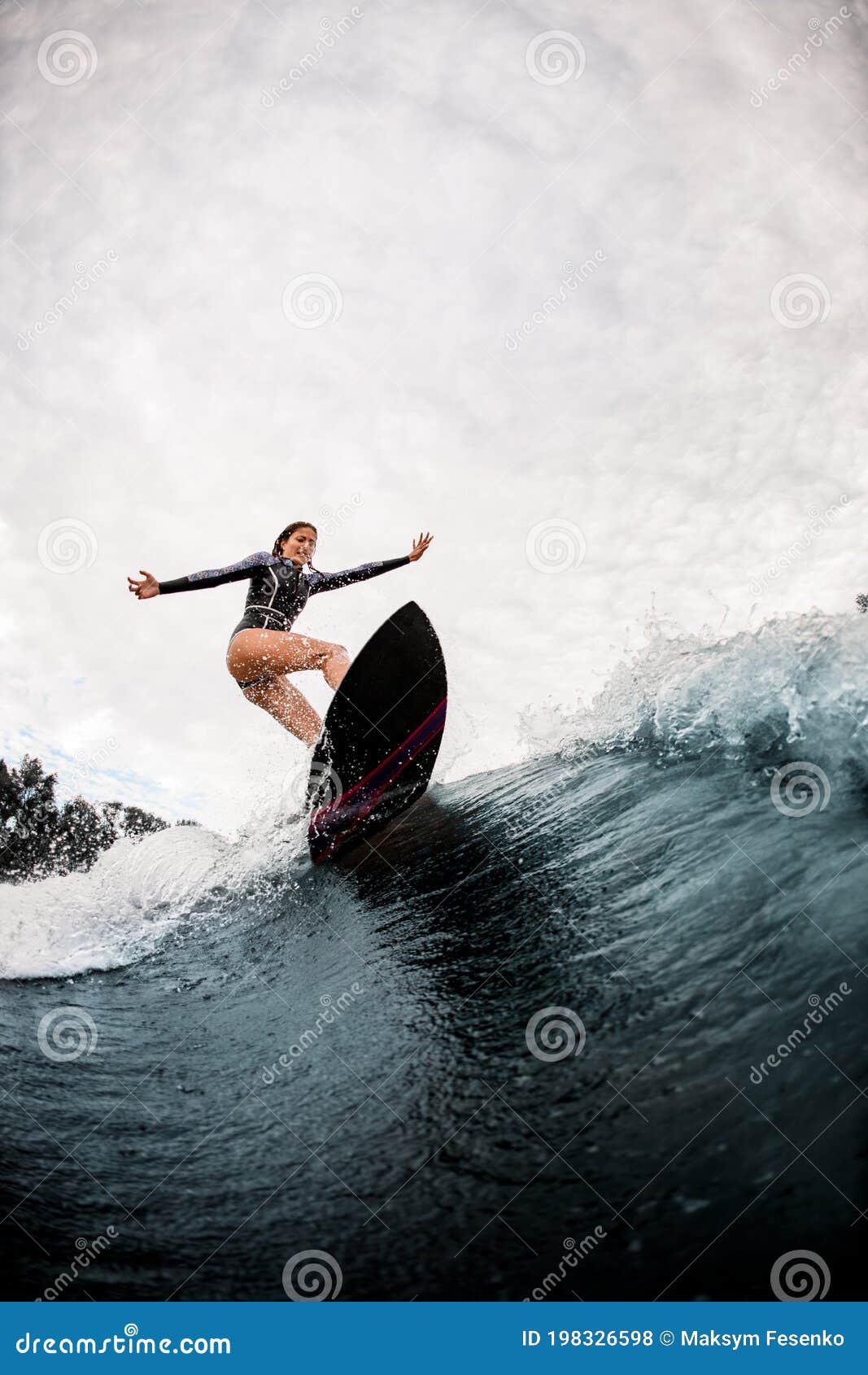 active woman in black wetsuit professionally rides on surf board on wave