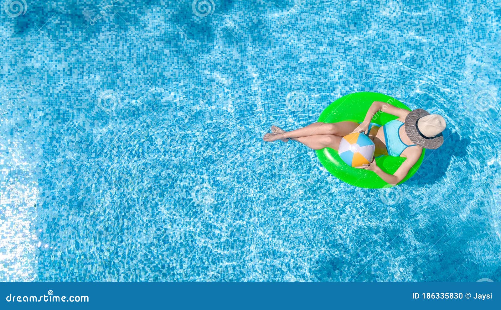 active young girl in swimming pool aerial top view from above, child relaxes and swims on inflatable ring donut and has fun