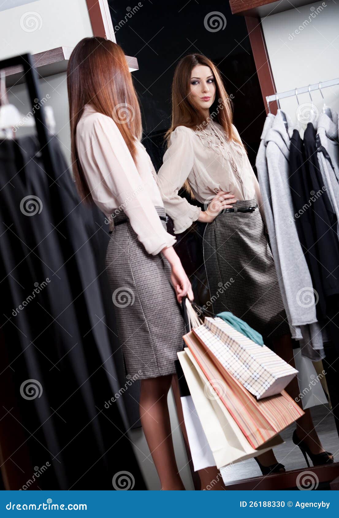 Admiring herself at the mirror. Woman admires herself at the mirror in the store while handing packets with purchases