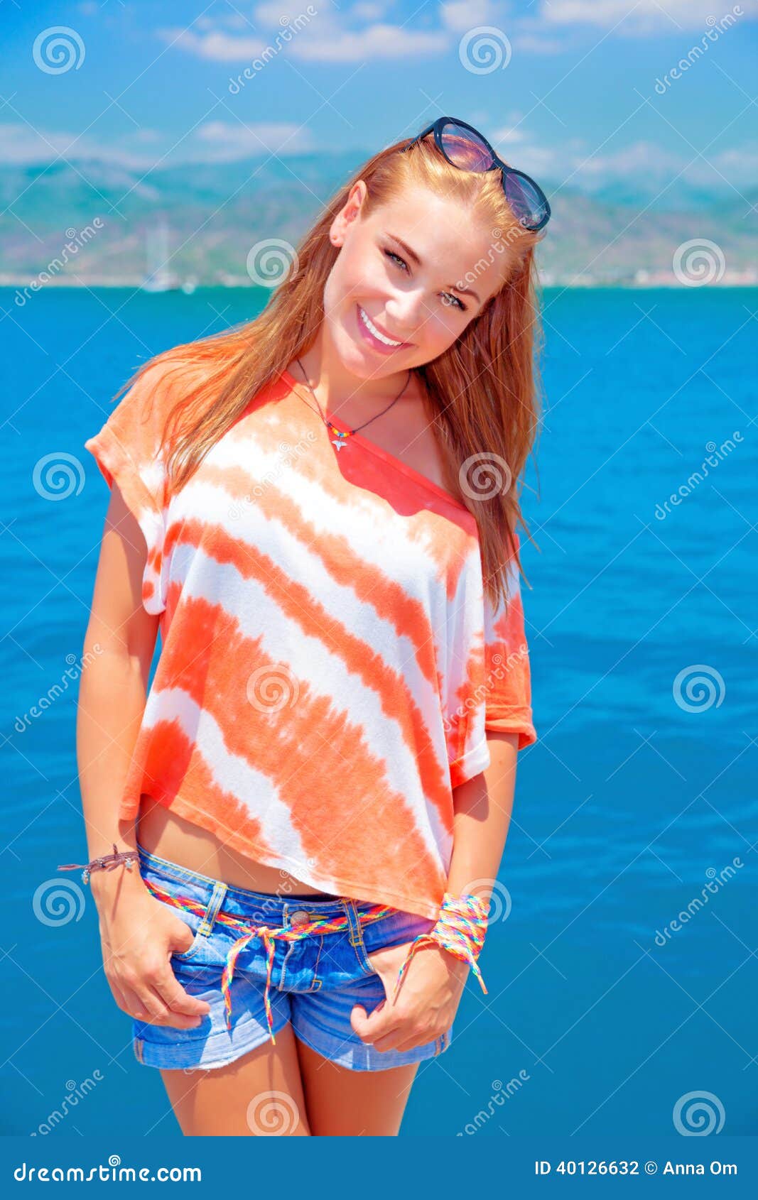Adolescente lindo el vacaciones de verano. Retrato de la muchacha adolescente linda que se coloca en fondo azul del mar, teniendo la diversión en la playa, vacaciones de verano y concepto de los días de fiesta