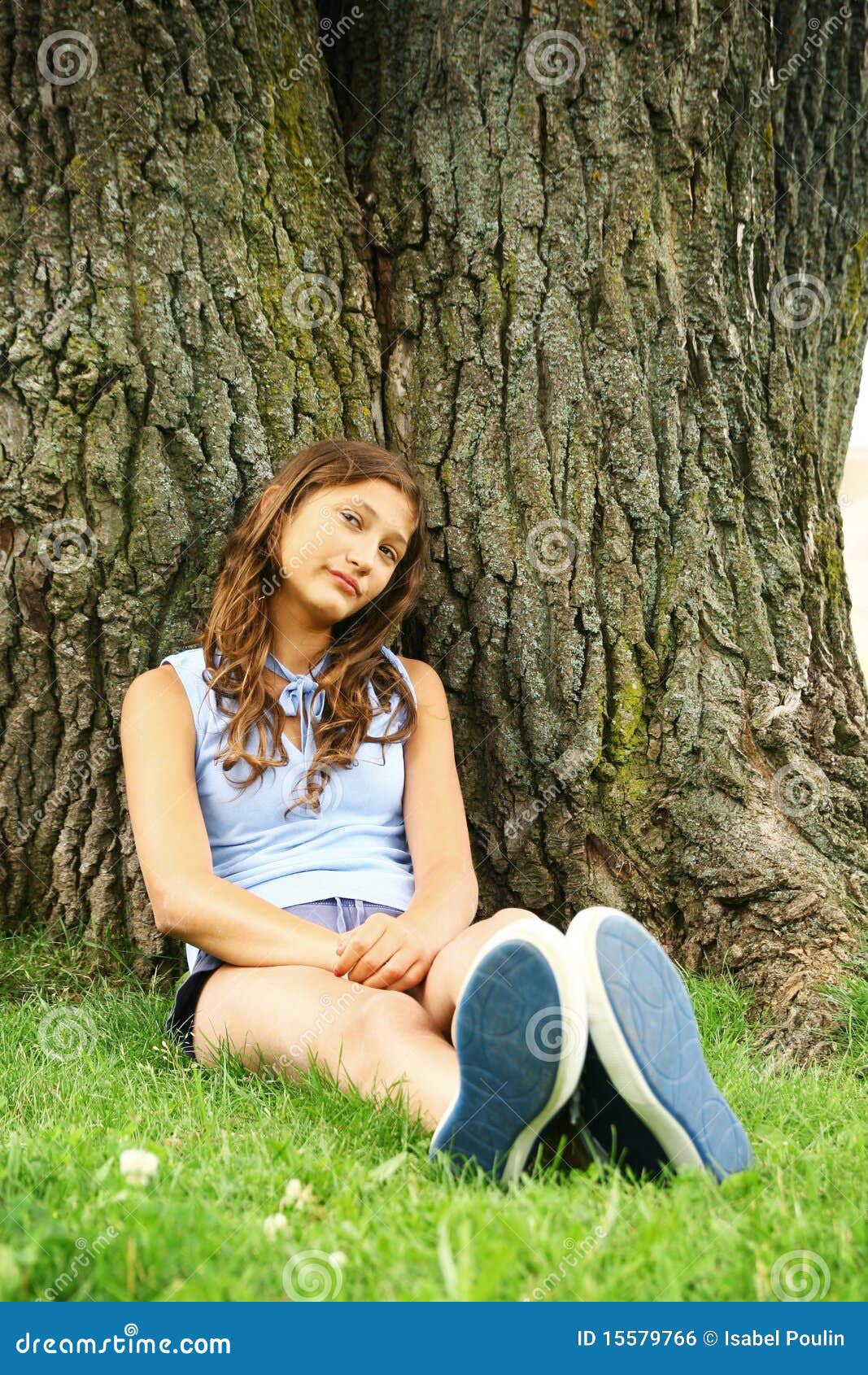 Adolescente sente-se em uma árvore. O adolescente bonito senta-se em uma grama em uma árvore enorme e velha.