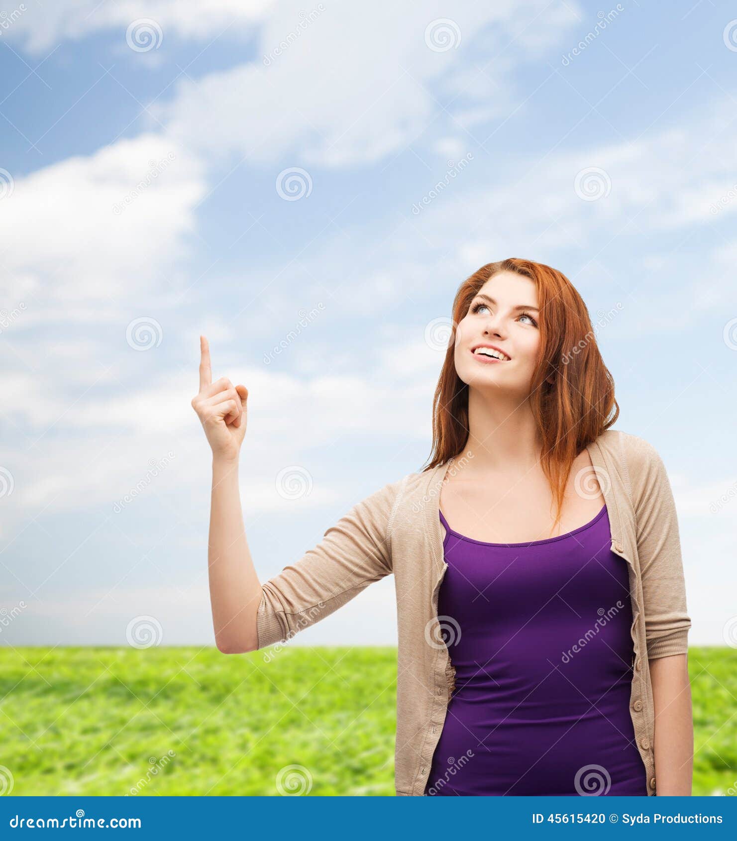 Adolescente sorridente che indica dito su. Concetto della natura, di estate, di gesto e della gente - adolescente sorridente in abbigliamento casual che indica dito su sopra il fondo dell'erba e del cielo blu