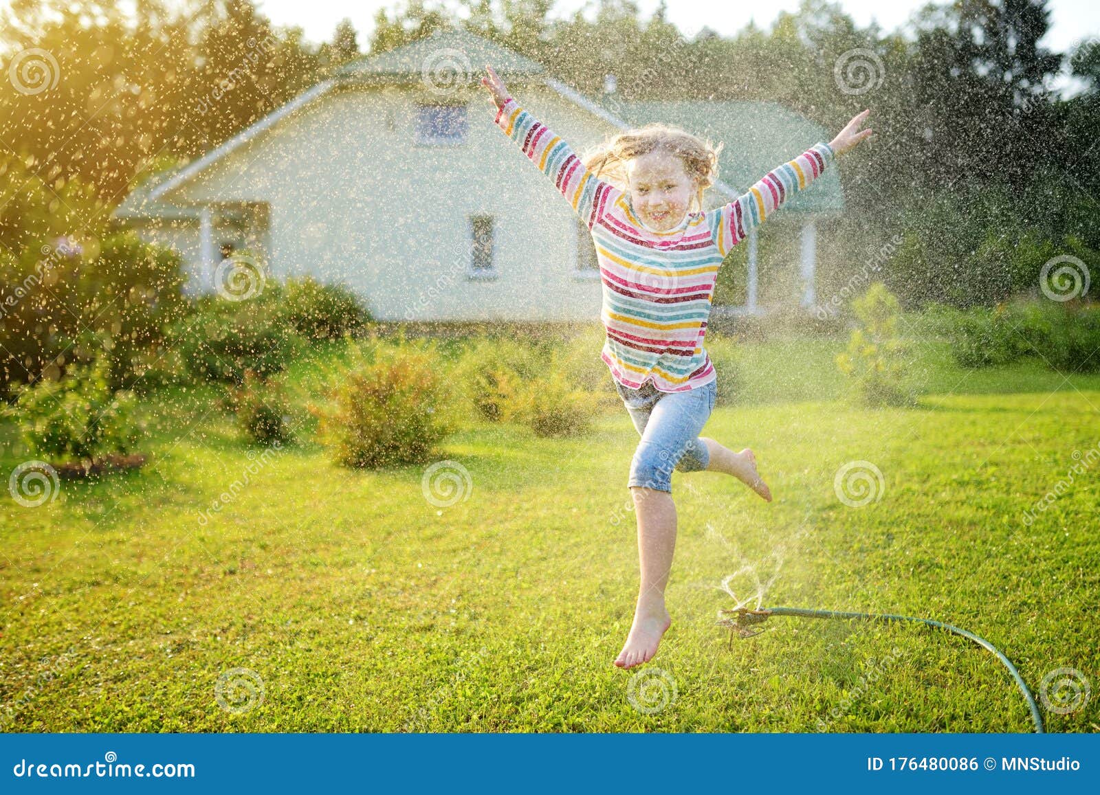 Adorable Girl Playing With A Sprinkler In A Backyard On 