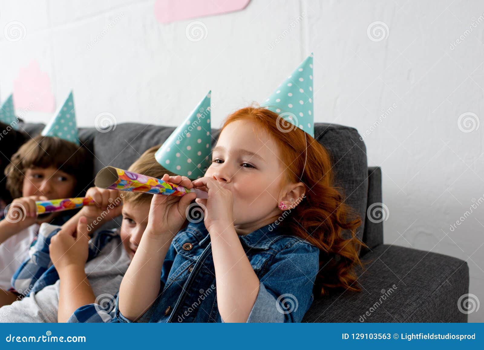 adorable little kids blowing in party blowers while sitting on sofa