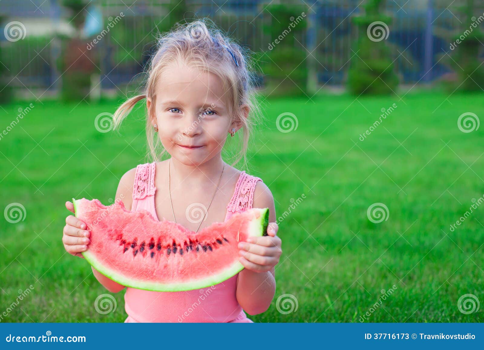 Adorable little toddler sitting on the grass with a piece of watermelon. This image has attached release.