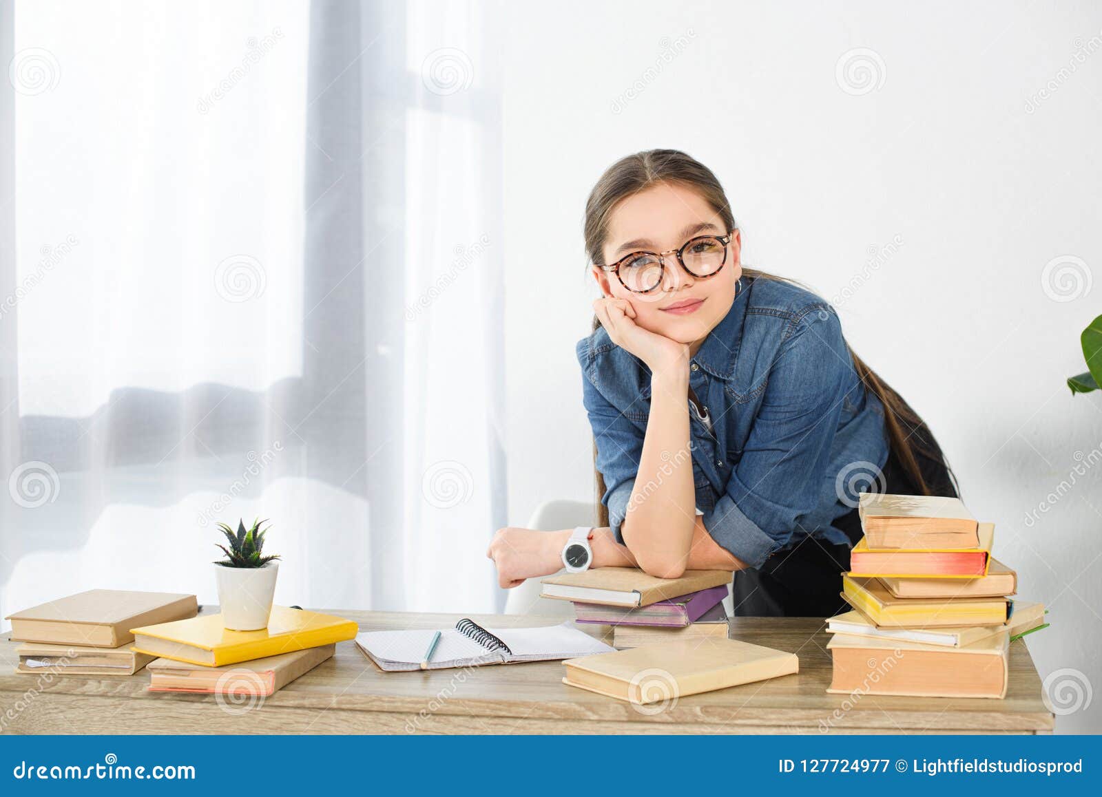 adorable preteen child resting chin on hand at table with books